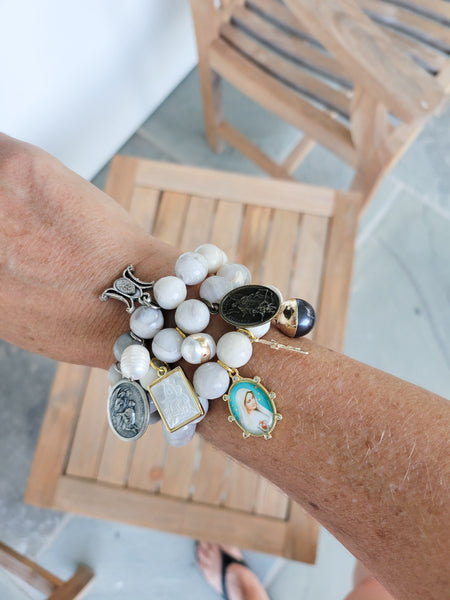 Close-up of a wrist wearing multiple bracelets with various charms on a wooden chair.